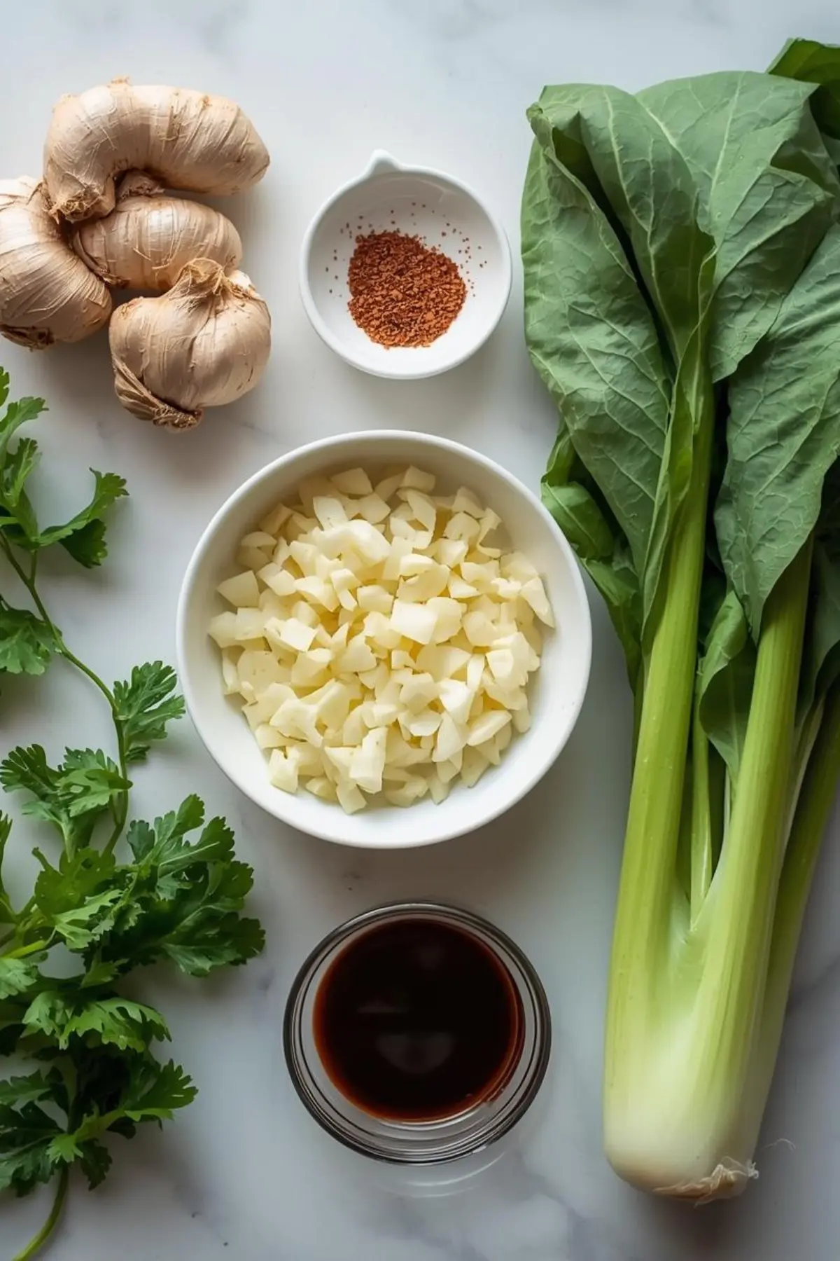 Fresh Asian ingredients including ginger, garlic, bok choy, and soy sauce arranged on marble counter
