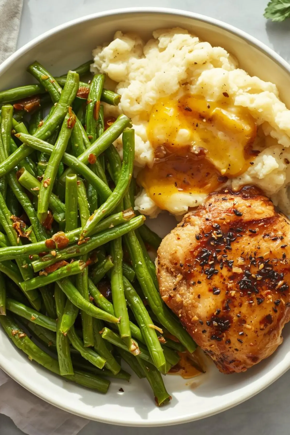 Canned green beans served on a white plate next to chicken and mashed potatoes